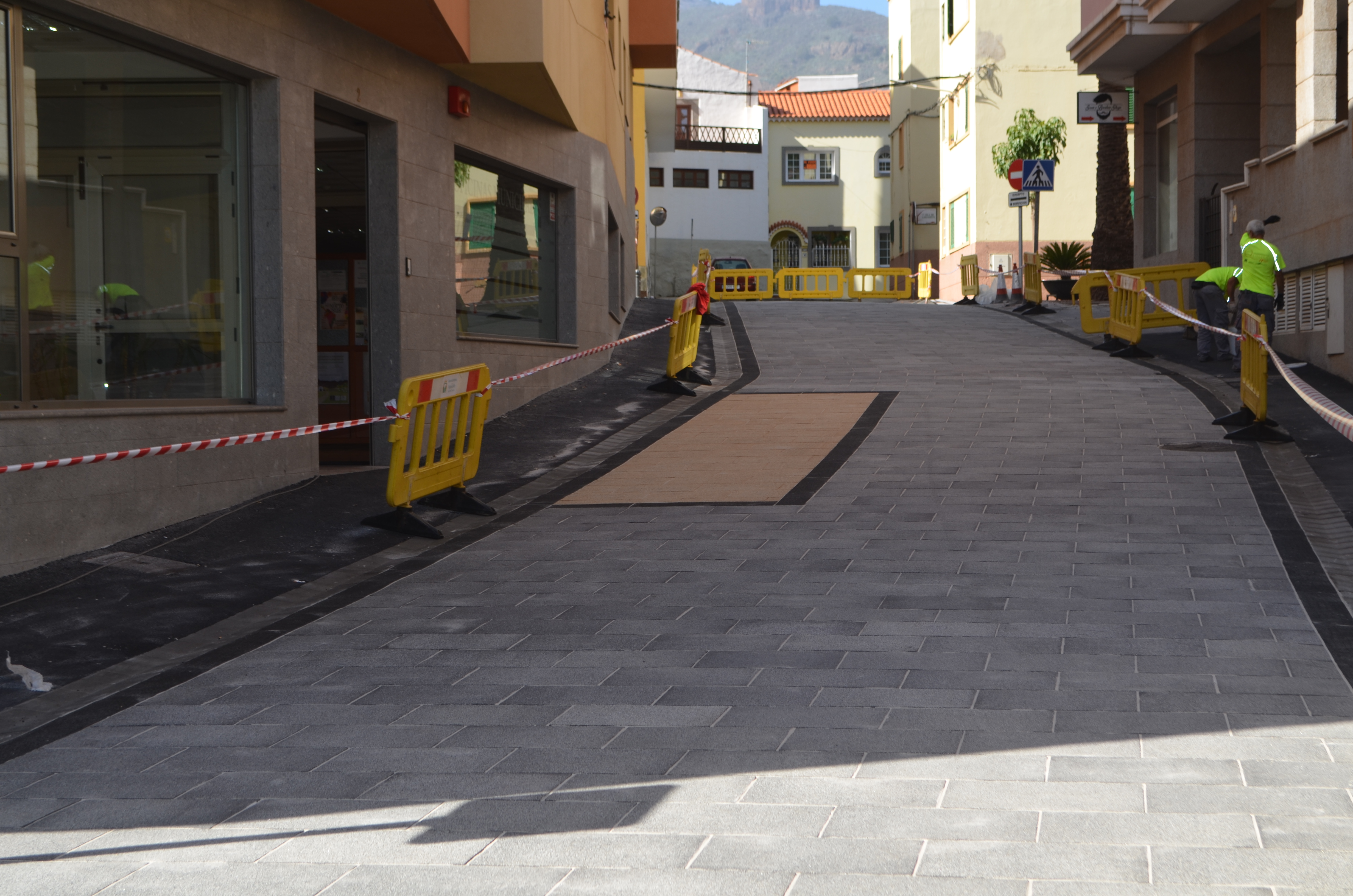 Calle urbana de Valsequillo con calzada de baldosas grises Zoruflex Preformado, banda clara central y vallas de obra Calle urbana de Valsequillo con calzada de baldosas grises Zoruflex Preformado, banda clara central y vallas de obra