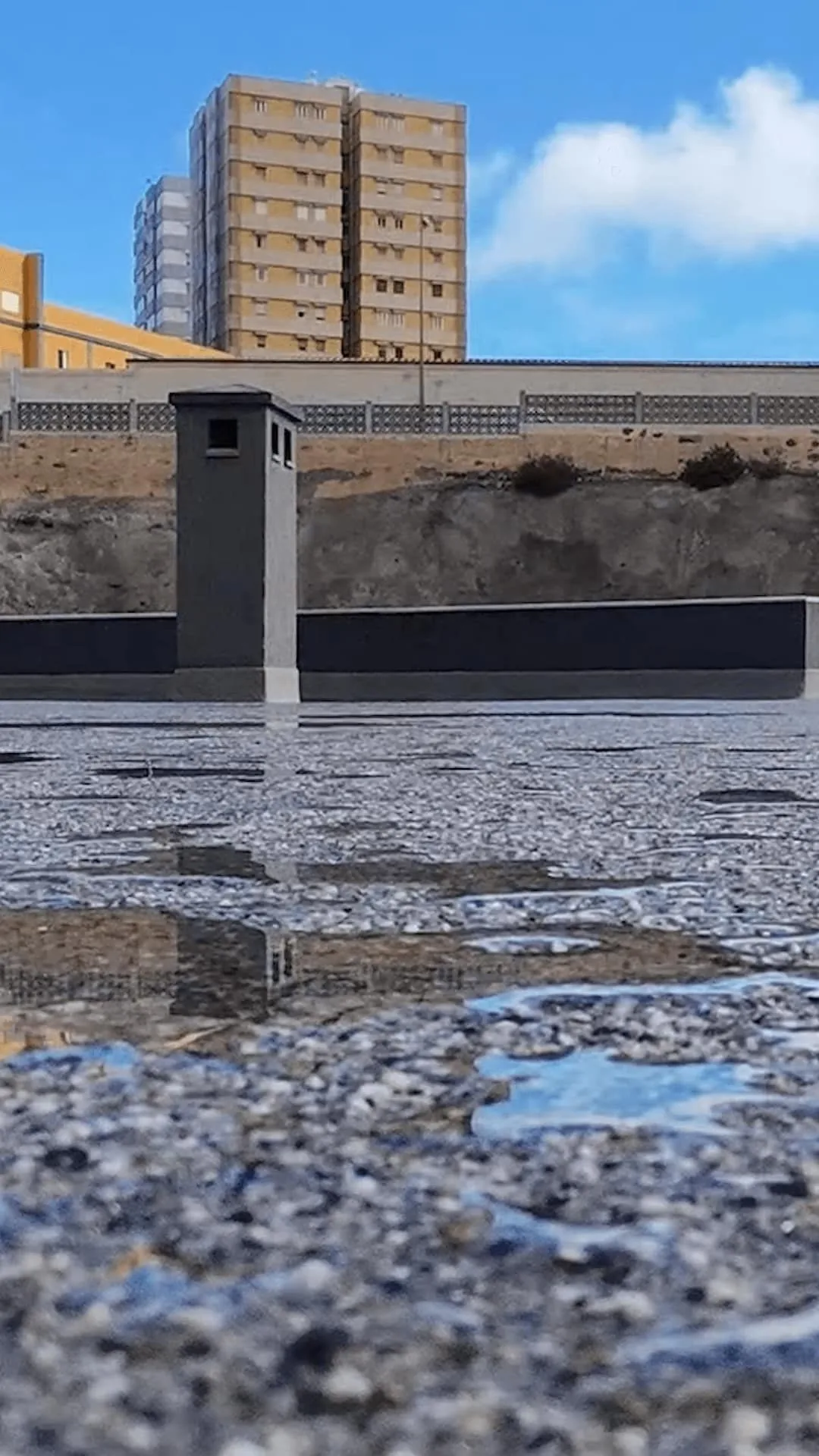 Superficie impermeabilizada con lámina de agua y entorno urbano al fondo