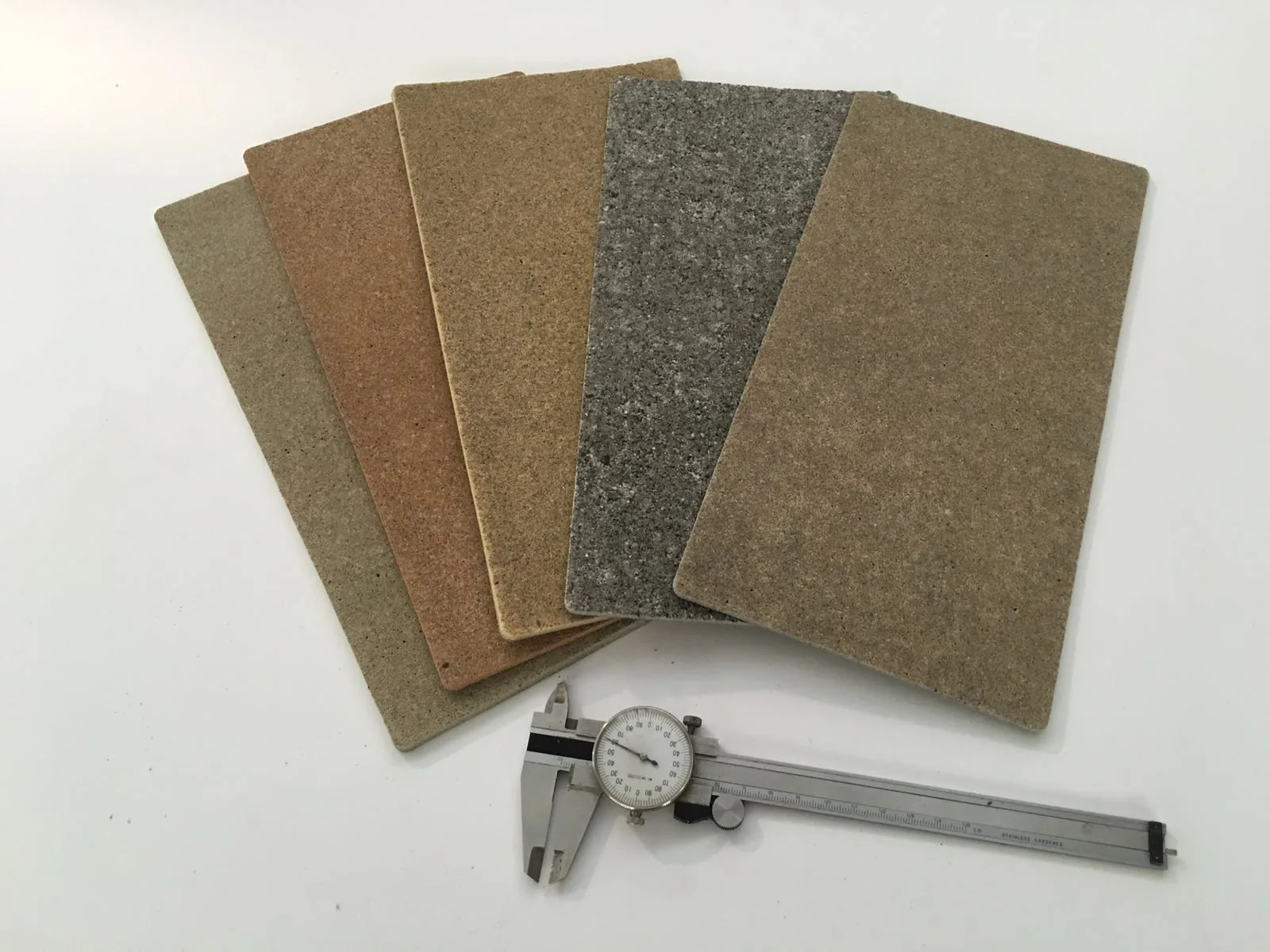 Cinco baldosas Zoruflex en distintos colores y texturas junto a un calibre que muestra su espesor reducido
