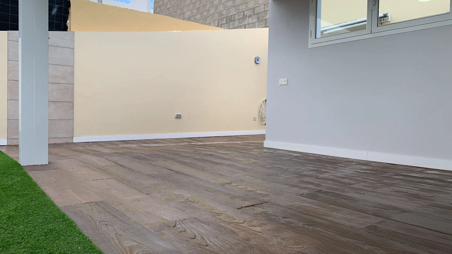 Patio exterior pavimentado con baldosa Zoruflex acabado madera junto a césped artificial